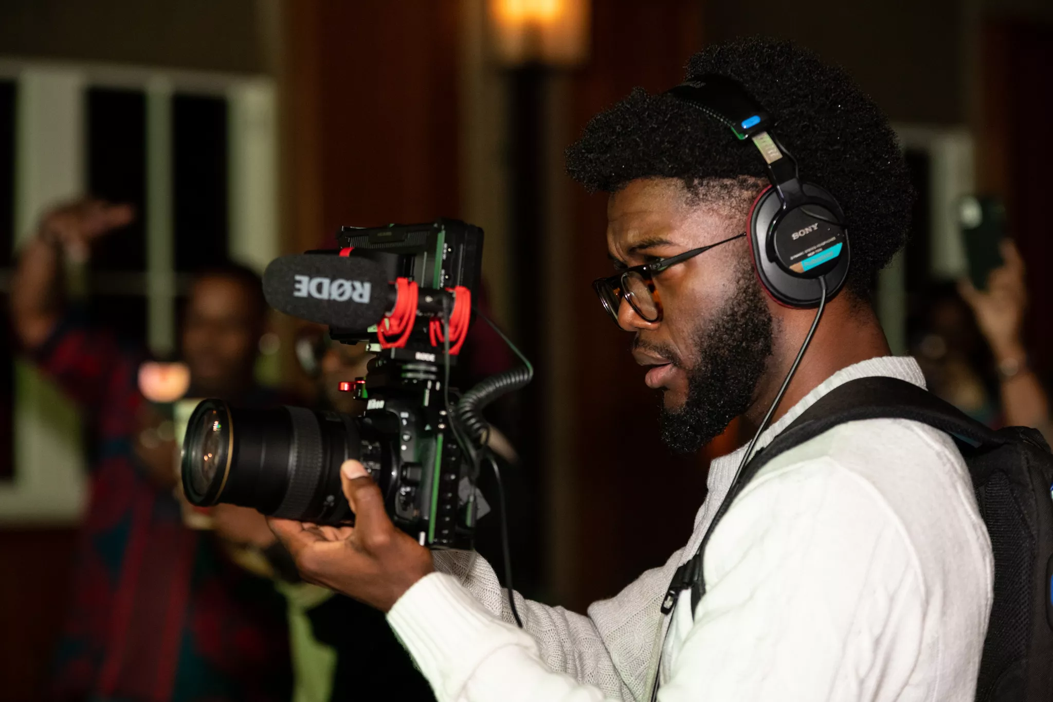 Videographer in headphones monitoring audio while filming at a crowded evening event.