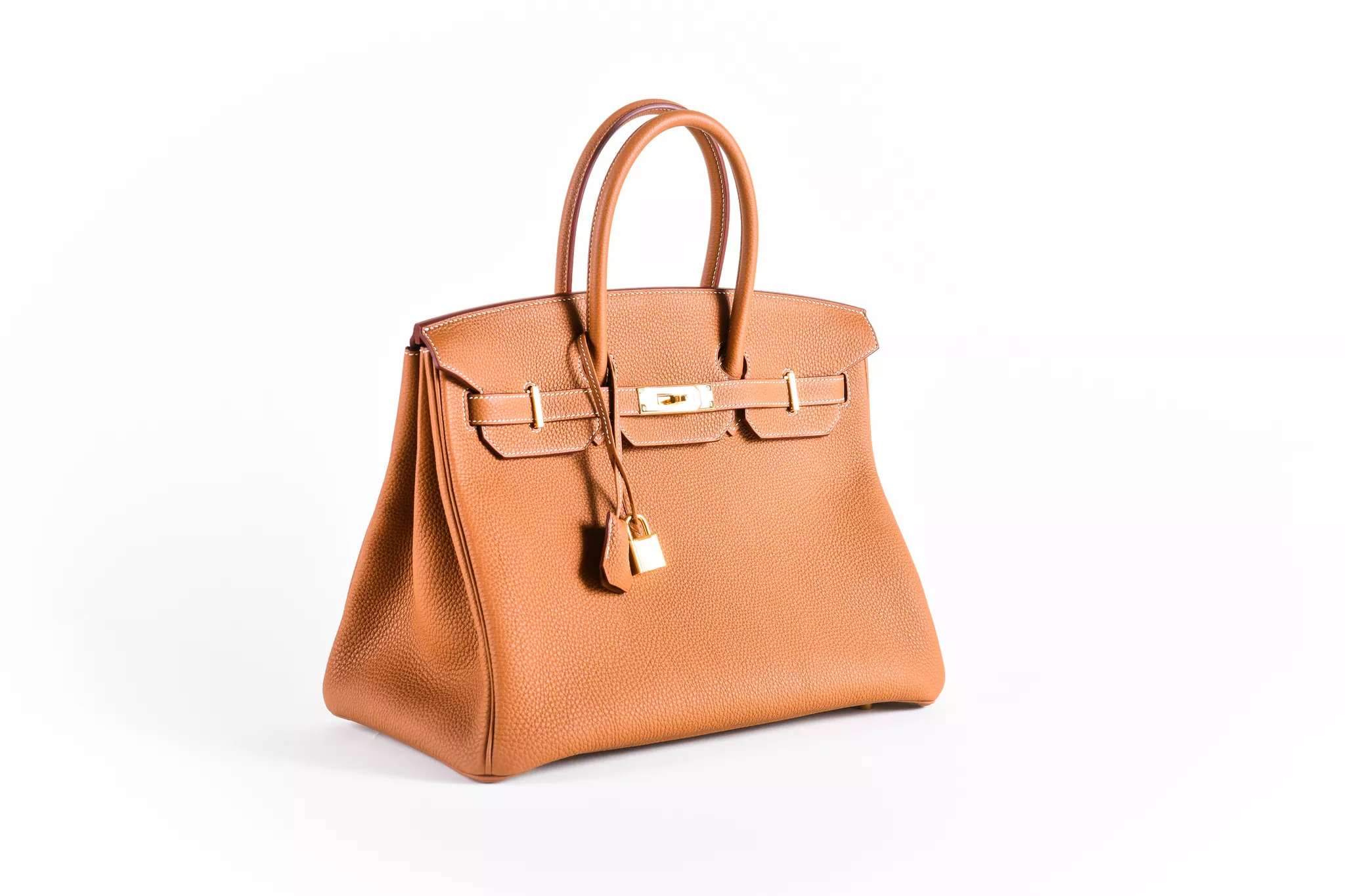 White-background product photography of a tan leather handbag with gold hardware.