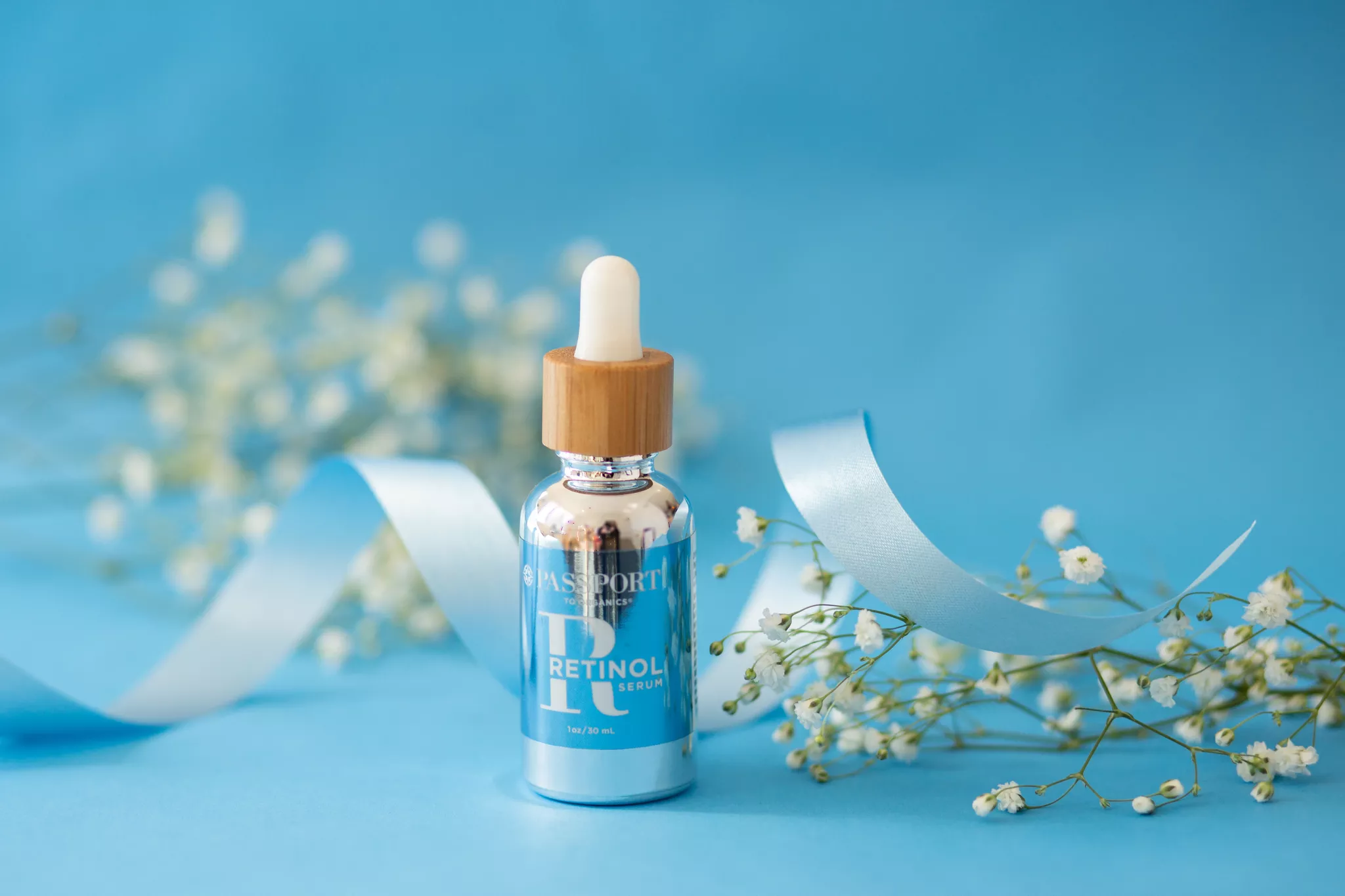 Styled product photography of a skincare serum bottle with flowers on a blue background.