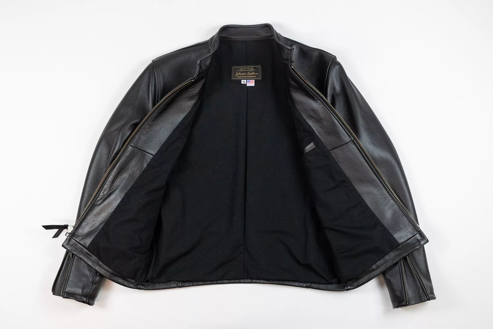Product photography of a black leather jacket laid flat to show its lining on white.