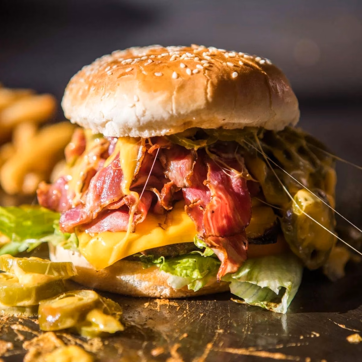 Pastrami and bacon cheeseburger with melted cheddar and crinkle-cut fries, shot in moody light for a delivery menu