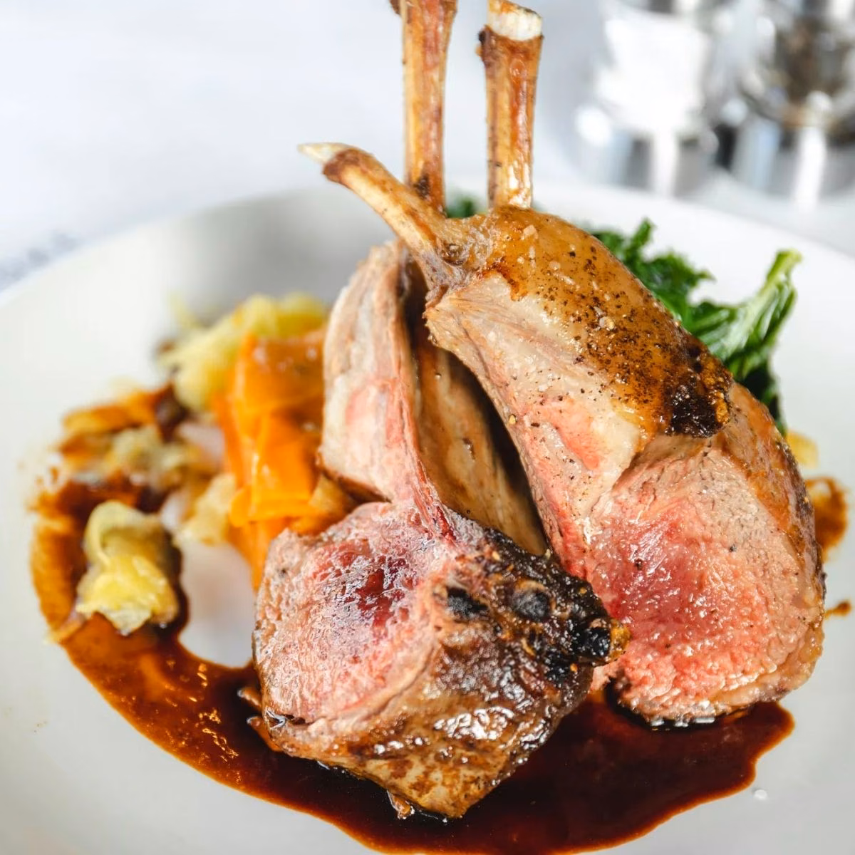 Rack of lamb cooked medium-rare with red wine jus and wilted greens, plated for fine-dining menu photography
