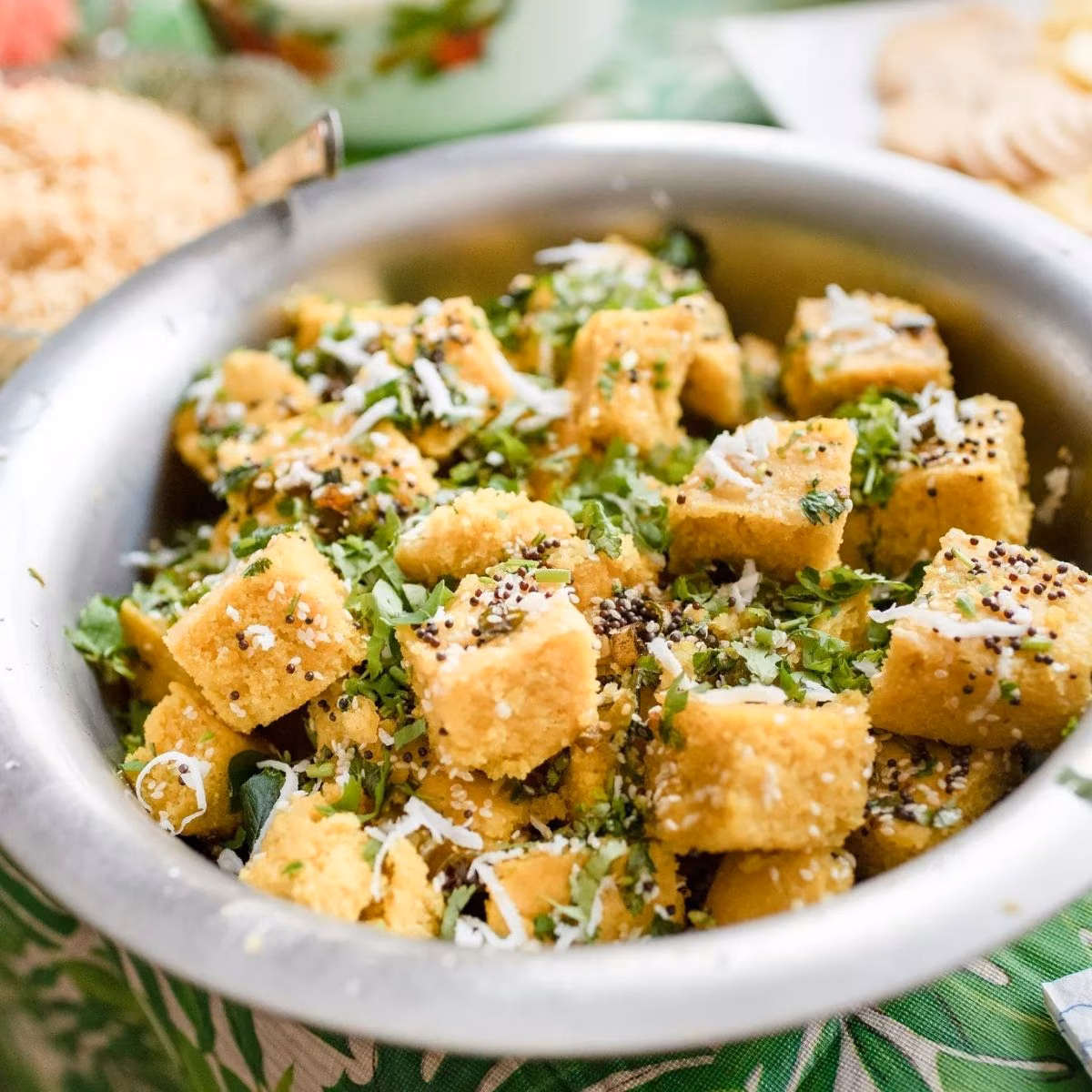 Bowl of steamed dhokla garnished with cilantro, mustard seeds and grated coconut, styled for an Indian restaurant menu
