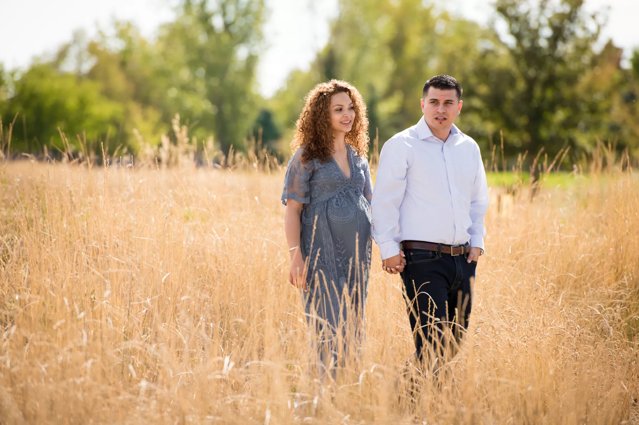 Engagement photo poses in motion — couple walking hand in hand through tall golden grass