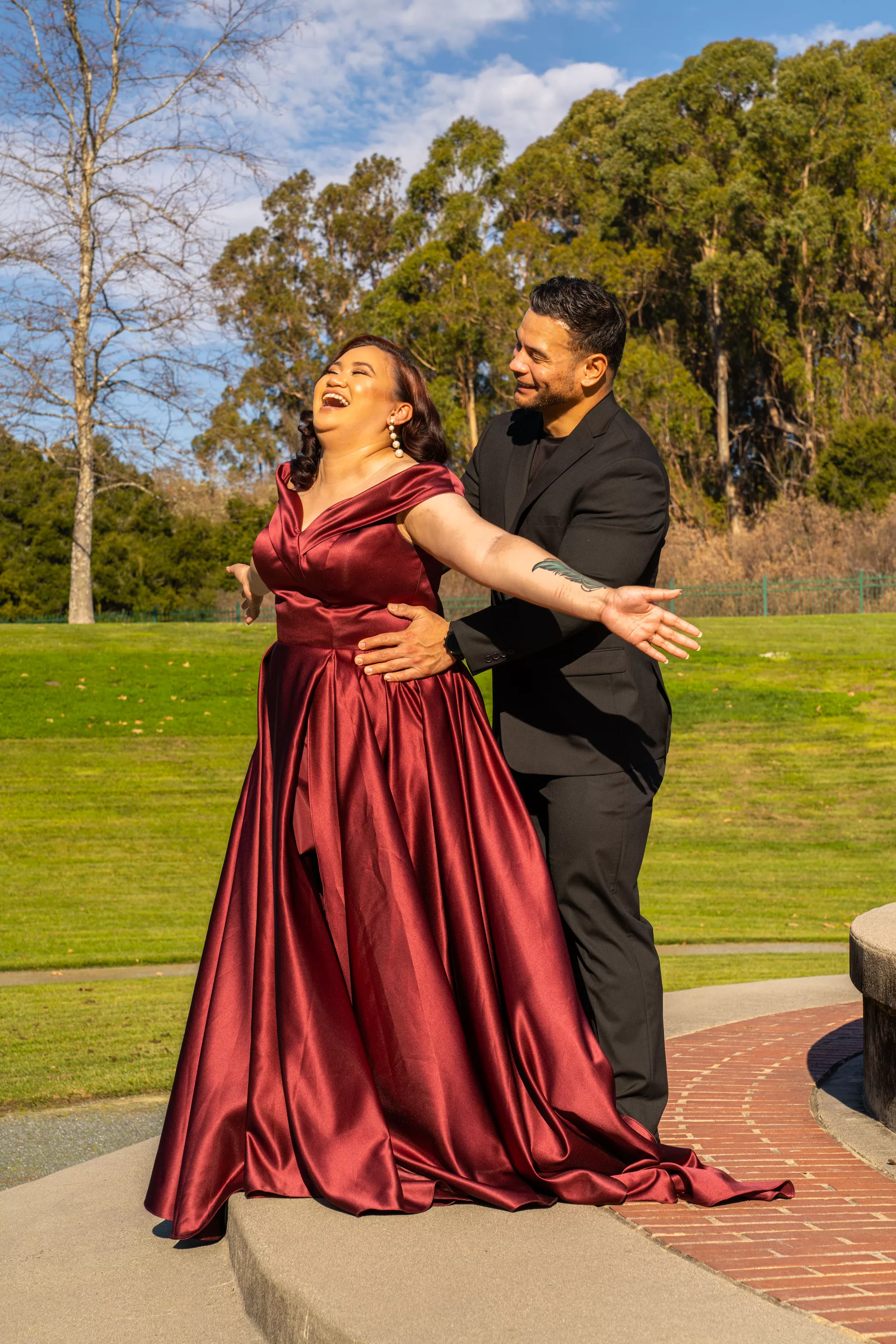 Prom poses for couples — laughing in a burgundy gown on a step, her partner behind her