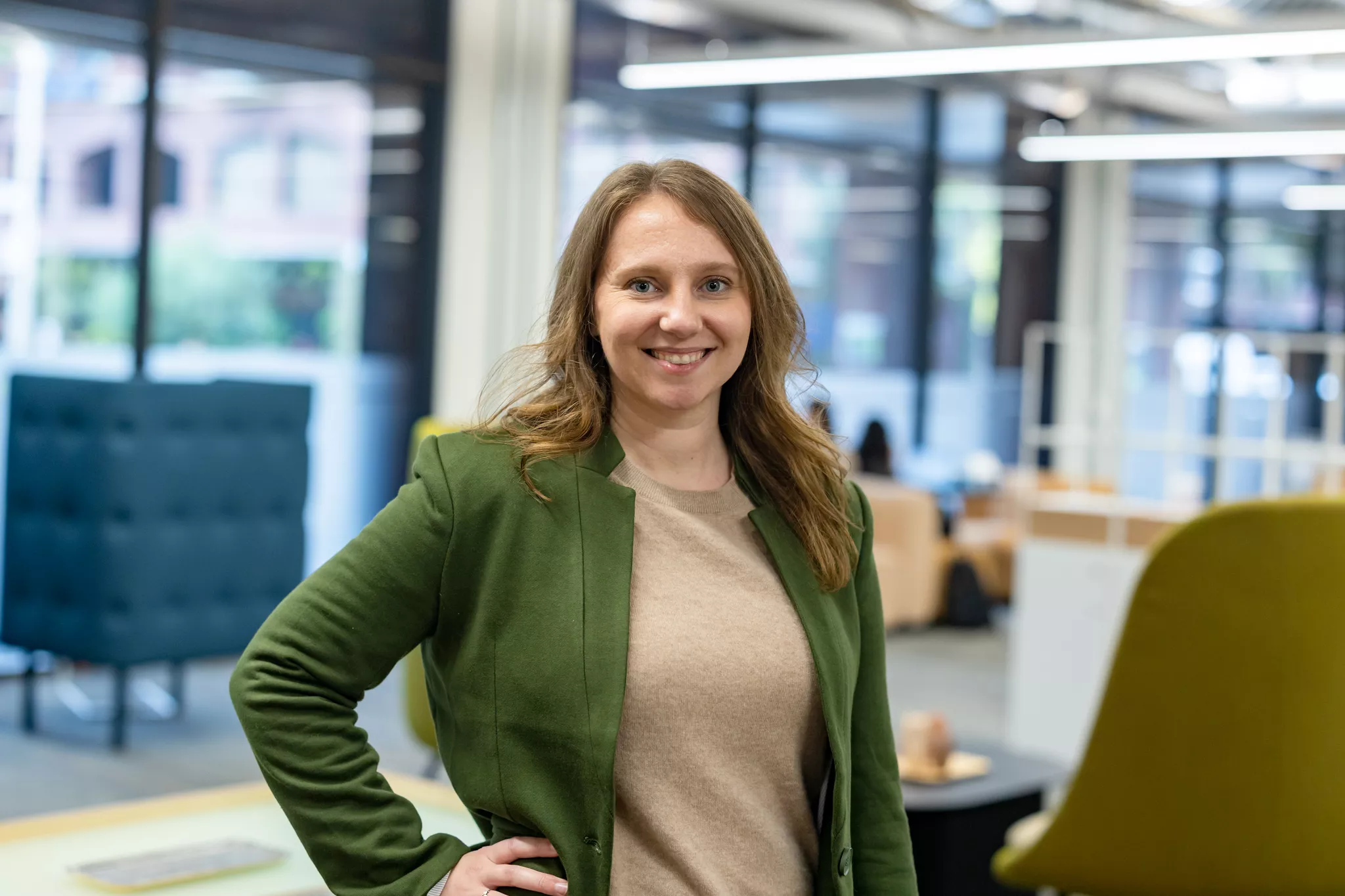 Headshot poses in an open-plan office — green blazer, hand on hip, smiling at the lens