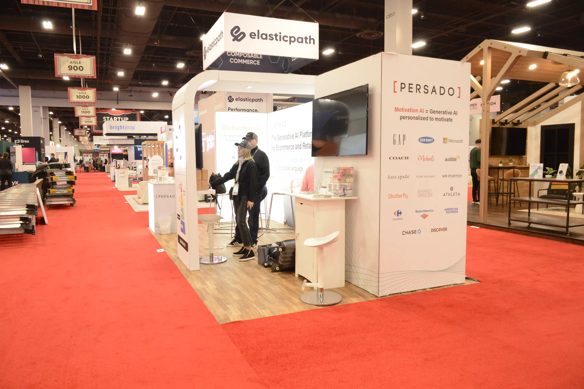 Attendees visit the Persado and Elastic Path booths on a red-carpeted trade show floor