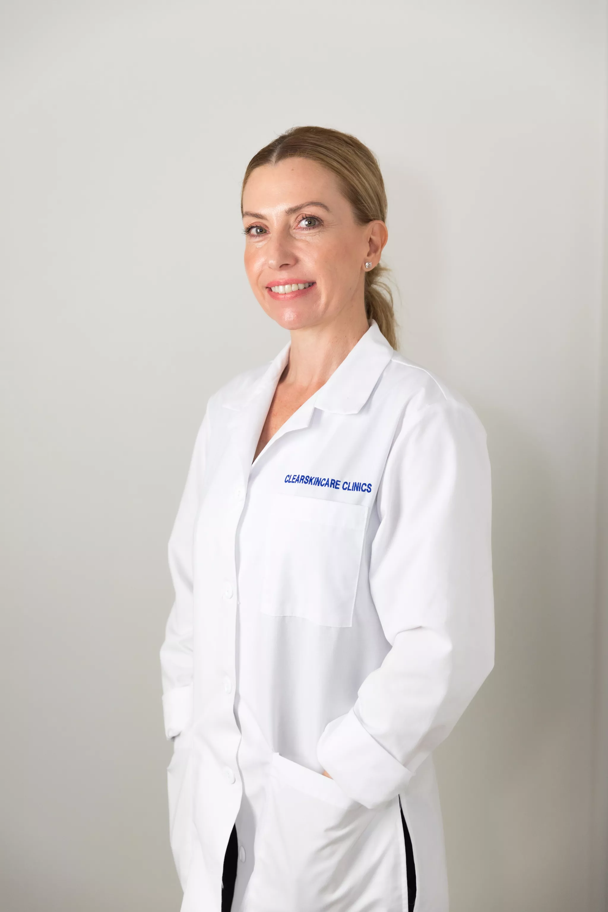 Clinician in a branded white lab coat, a corporate headshot on a plain neutral wall