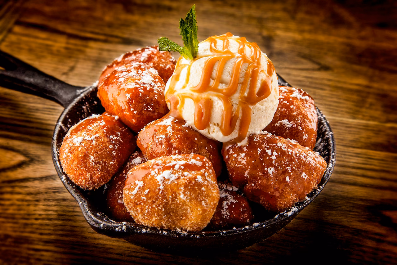 Cast iron skillet of fried dough bites topped with vanilla ice cream and caramel sauce