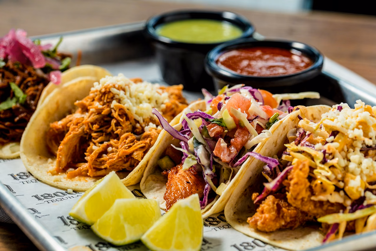 Tray of assorted street tacos with lime wedges and red and green salsas