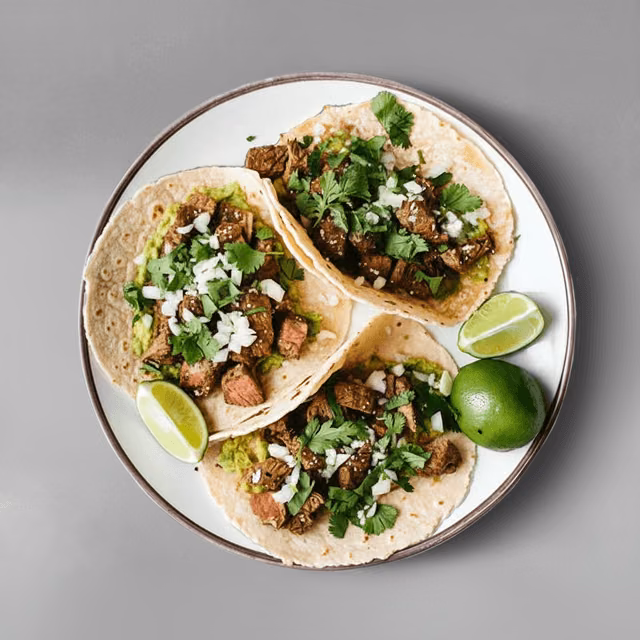 Three beef tacos topped with chopped cilantro and onions, served with lime wedges