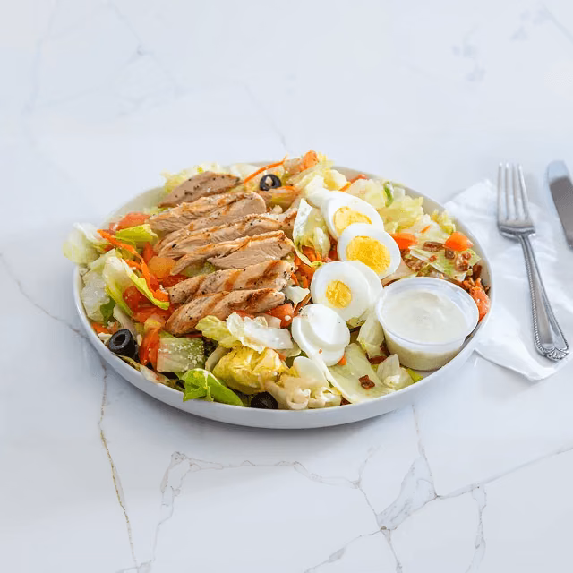 Grilled chicken salad with lettuce, tomatoes, hard-boiled eggs and creamy dressing on a white plate