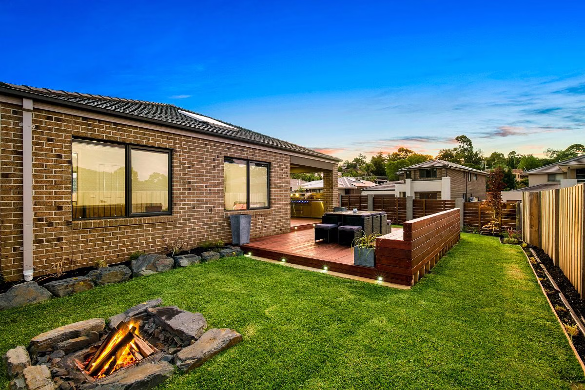 Professional real estate photo of a backyard at dusk with a deck, fire pit, and lawn