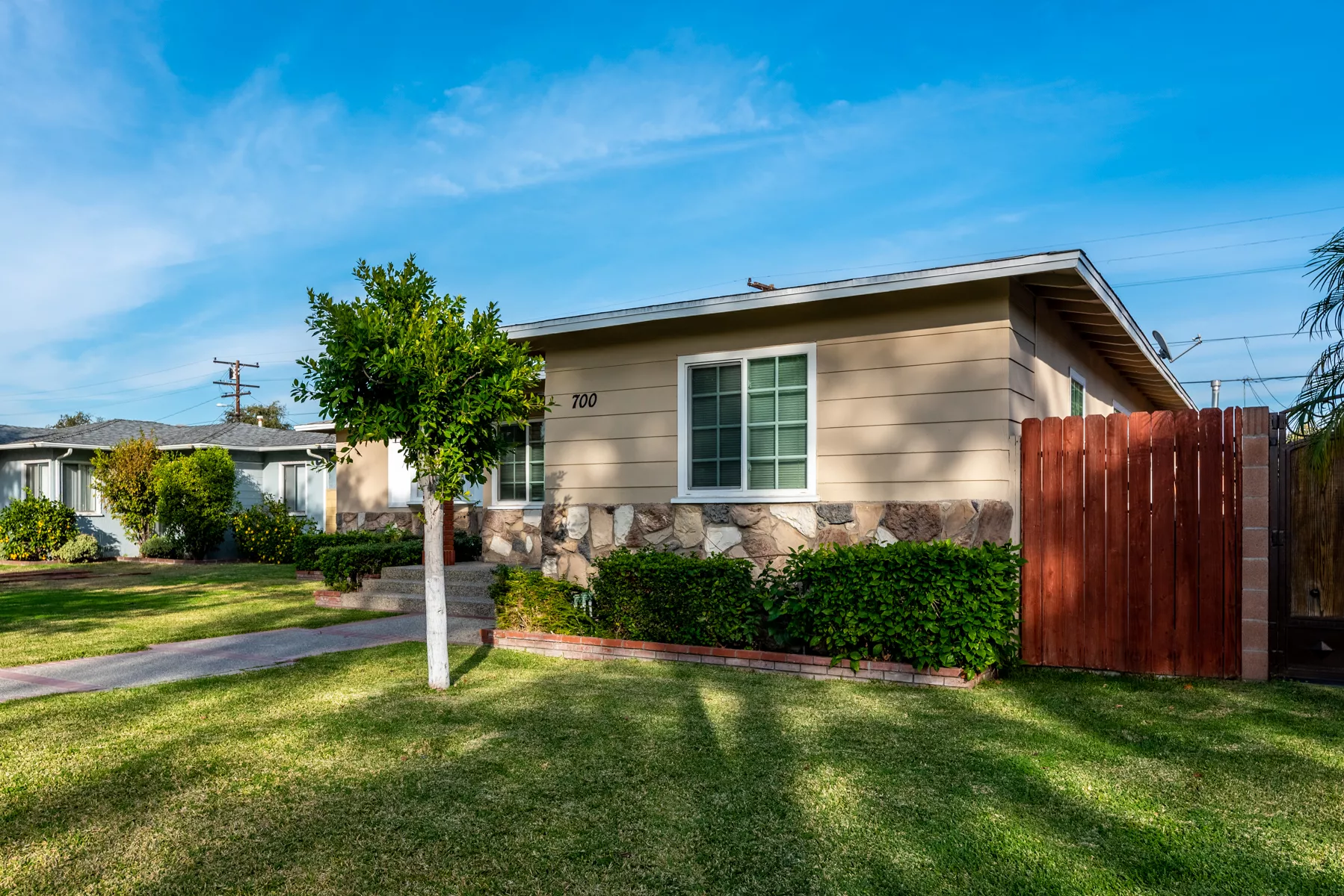 Real estate listing photo of a single-story ranch home with stone trim and sunlit front lawn