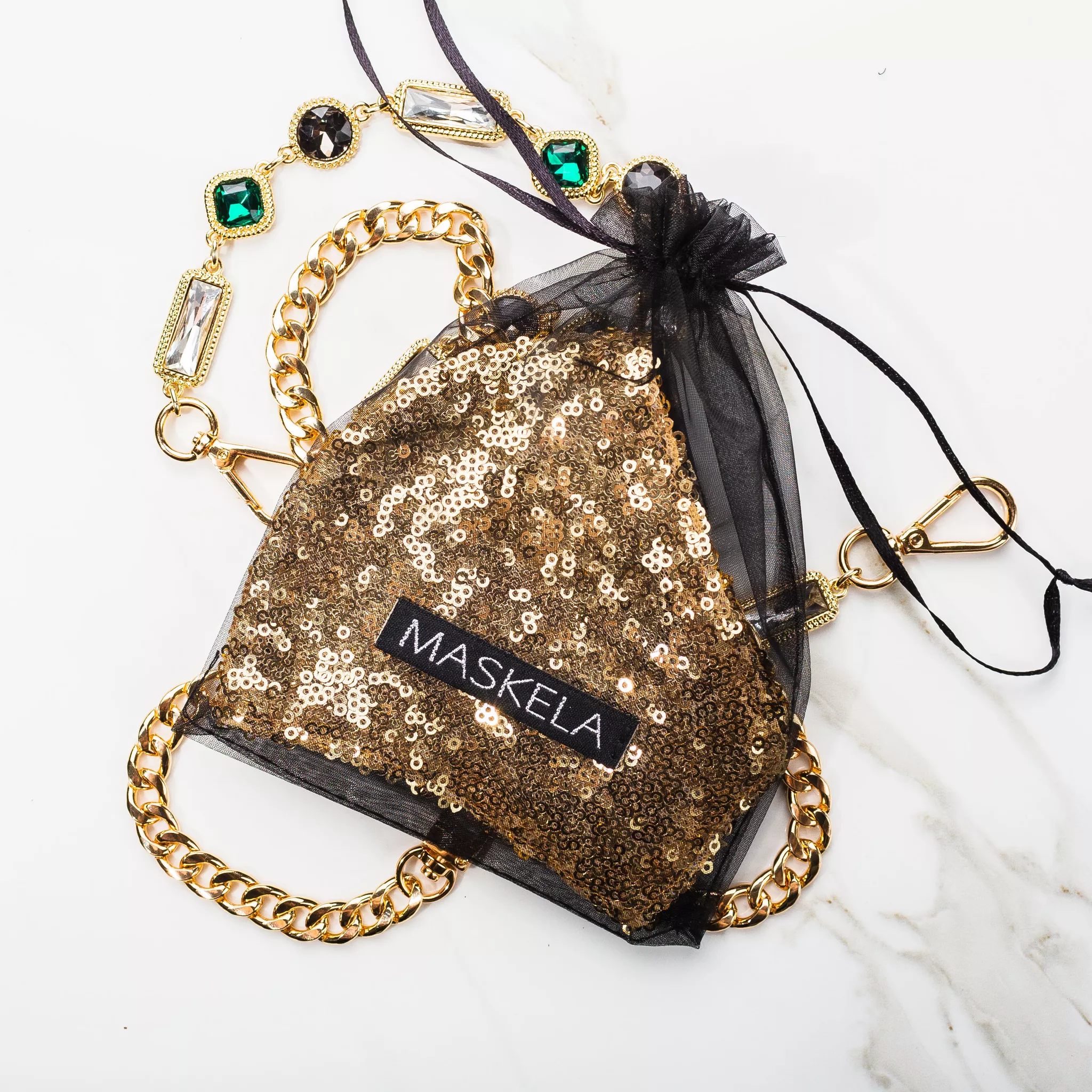 Flat lay photography of a gold sequin face mask, chain and jeweled necklace on white marble
