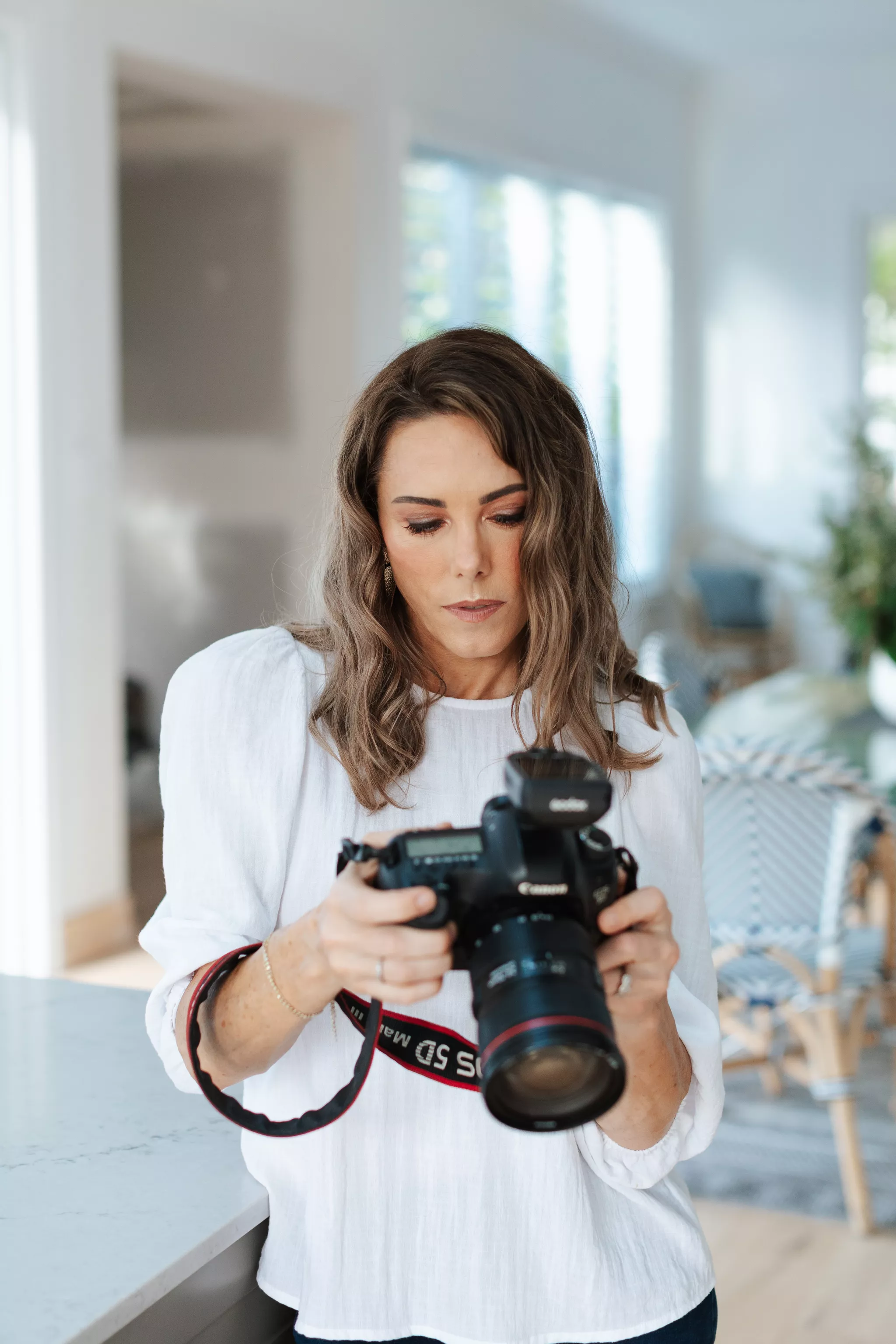 Real estate photographer reviewing shots on a Canon DSLR in a bright white kitchen