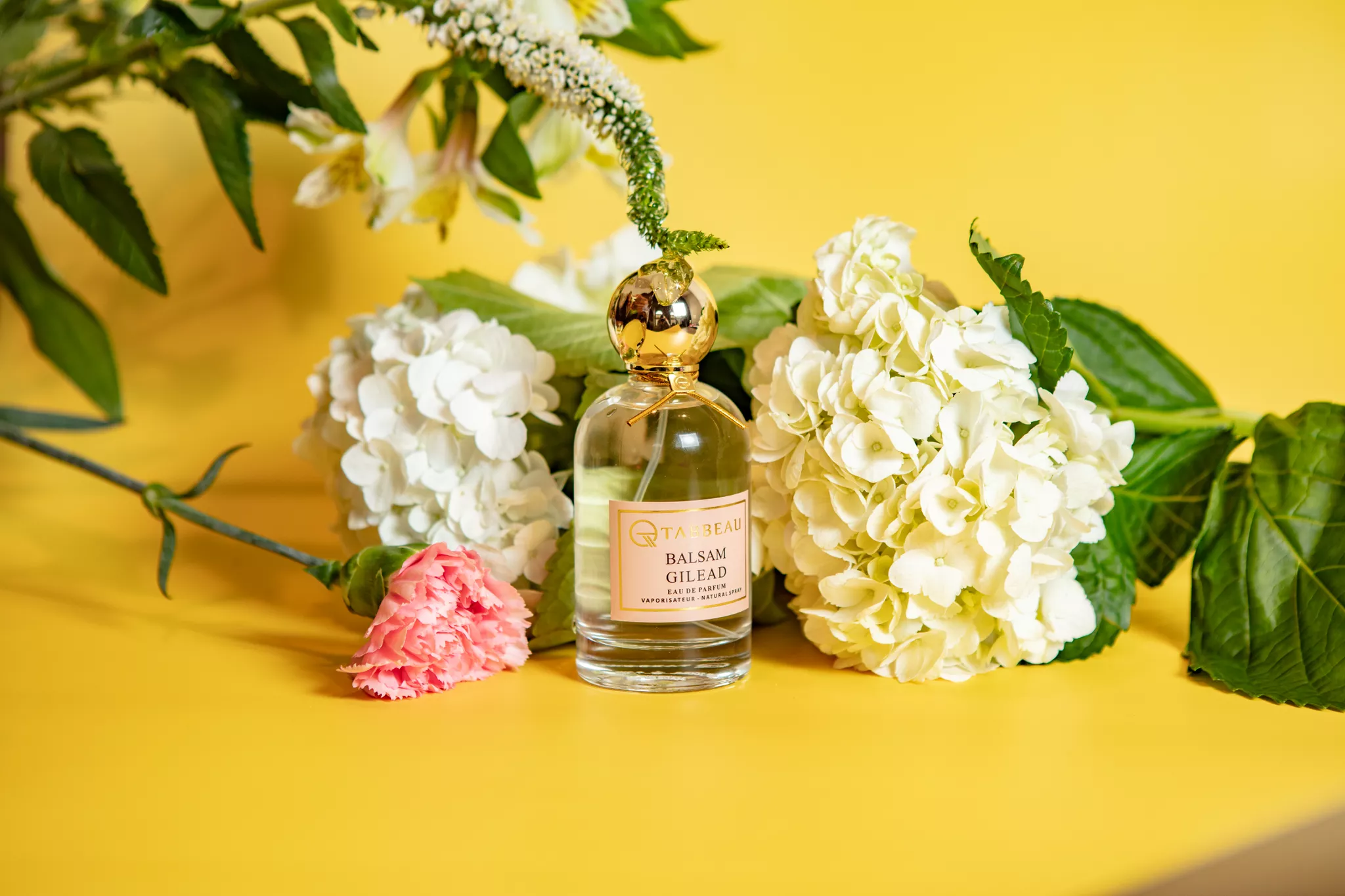 Product catalog photo of a perfume bottle with white hydrangeas on a yellow background