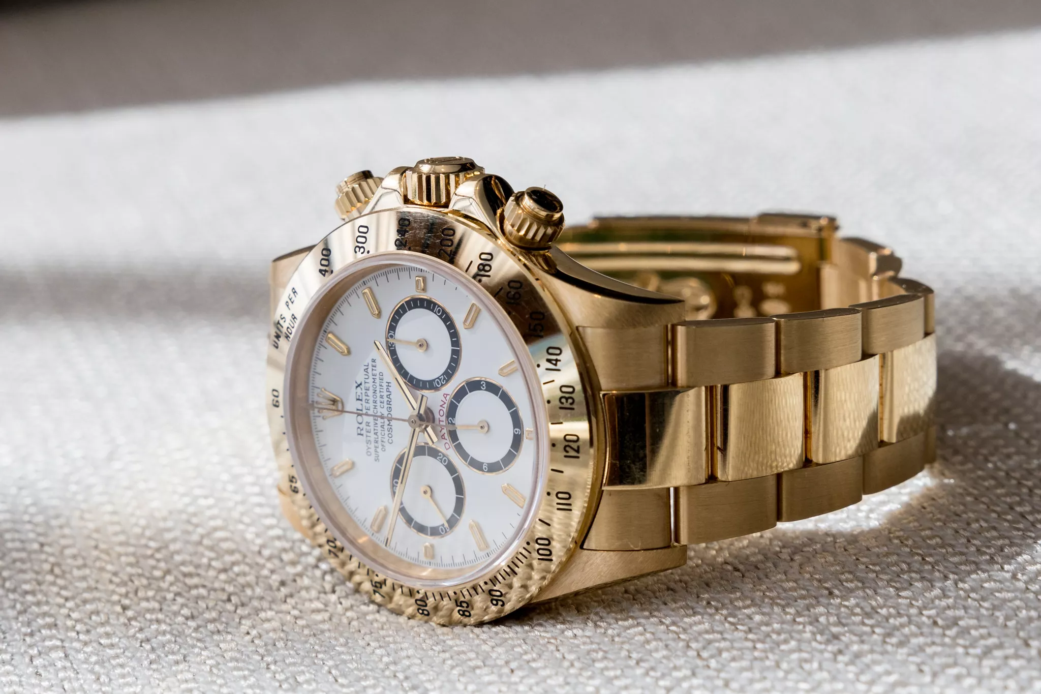 Product catalog photo of a gold chronograph watch on textured cream fabric