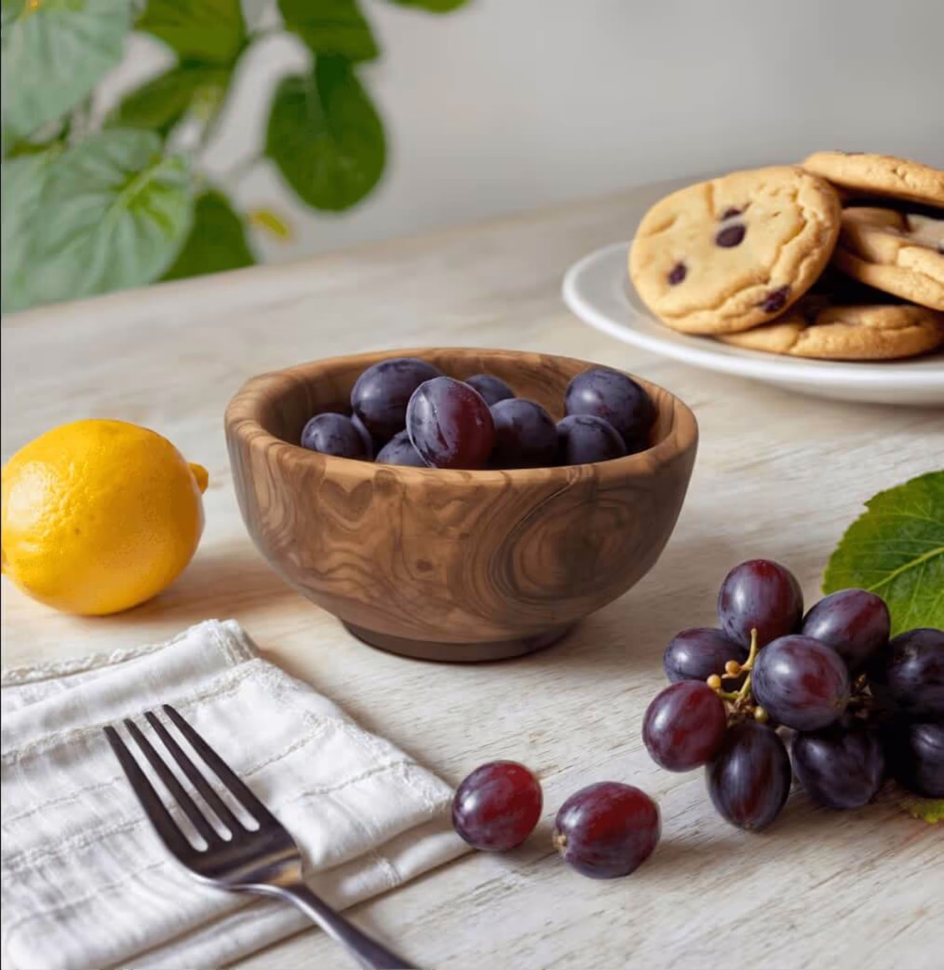 AI-generated food flatlay with grapes in a wooden bowl, lemon, and chocolate chip cookies representing generative AI photo solutions