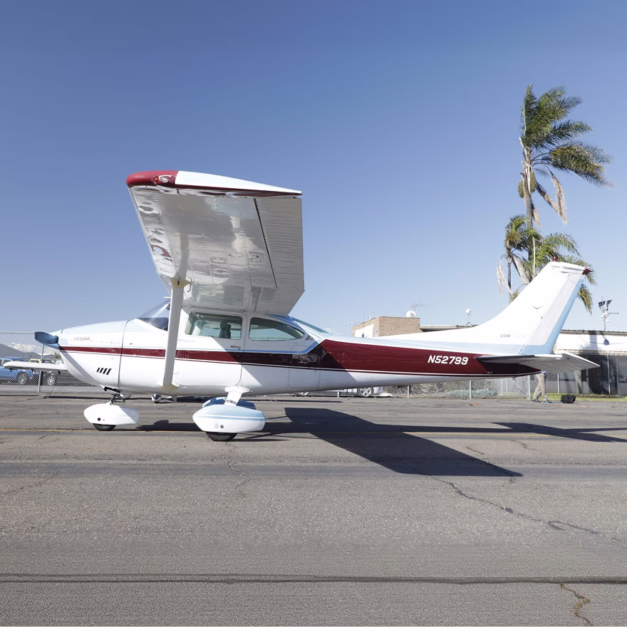Cessna small plane parked on a sunny airport tarmac with palm trees visible in the background.