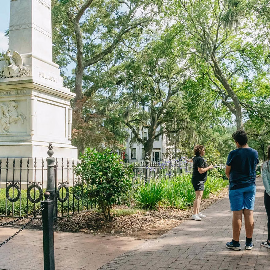 Two men walking along a pathway in a historic garden park near the Pulaski monument.
