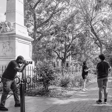 Photographer setting up an outdoor shoot with two men in a scenic historic park.
