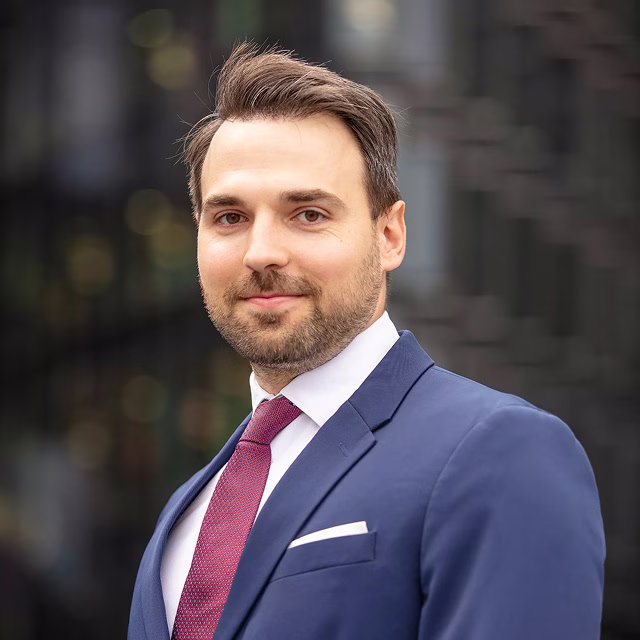 Young man in a navy suit and red tie posing for a professional portrait outdoors in the city.