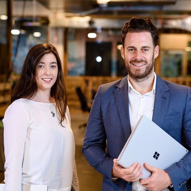 Man and woman smiling side by side in professional headshots taken inside a modern office.
