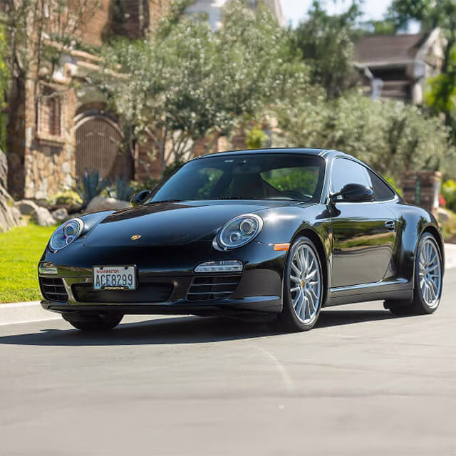 Black Porsche 911 parked on a residential street with greenery in the background