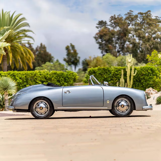 Vintage silver convertible parked in a driveway surrounded by palm trees
