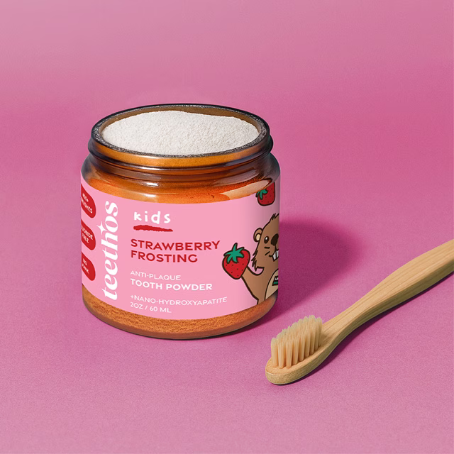 Kids holding strawberry tooth powder and bamboo toothbrushes in a pink-themed product shoot.