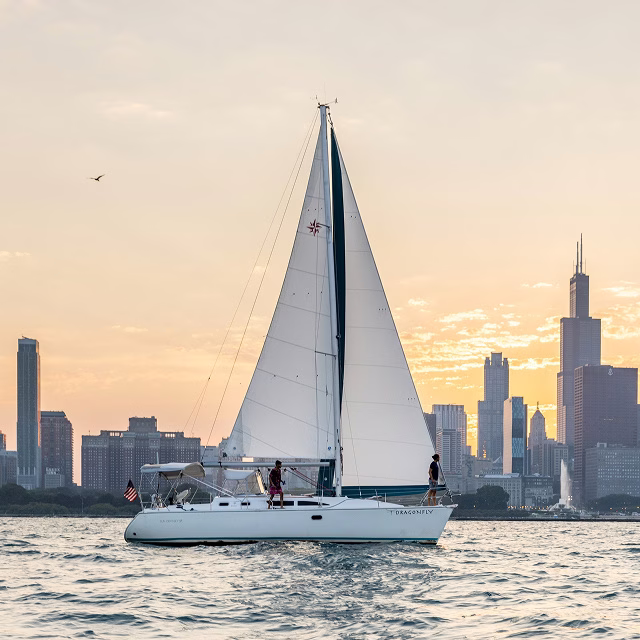 Sailboat on the water at golden hour with the Chicago city skyline glowing at sunset.
