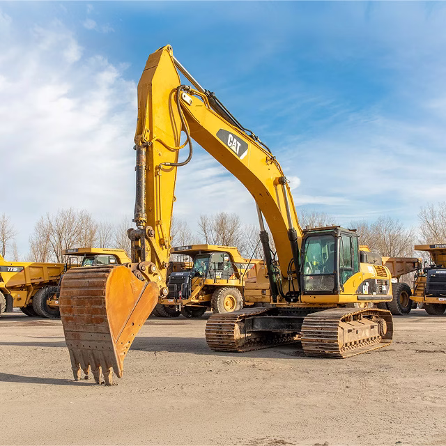 CAT excavator parked in a construction equipment yard under a clear blue sky.