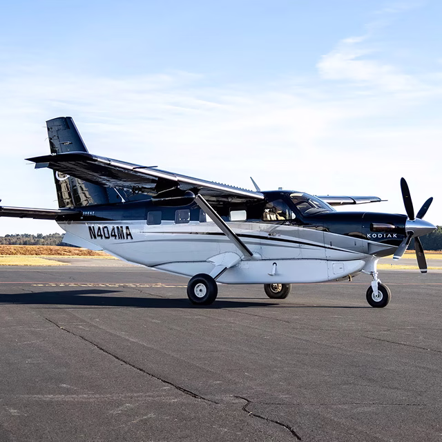 Kodiak turboprop aircraft parked on a tarmac at a small regional airport.
