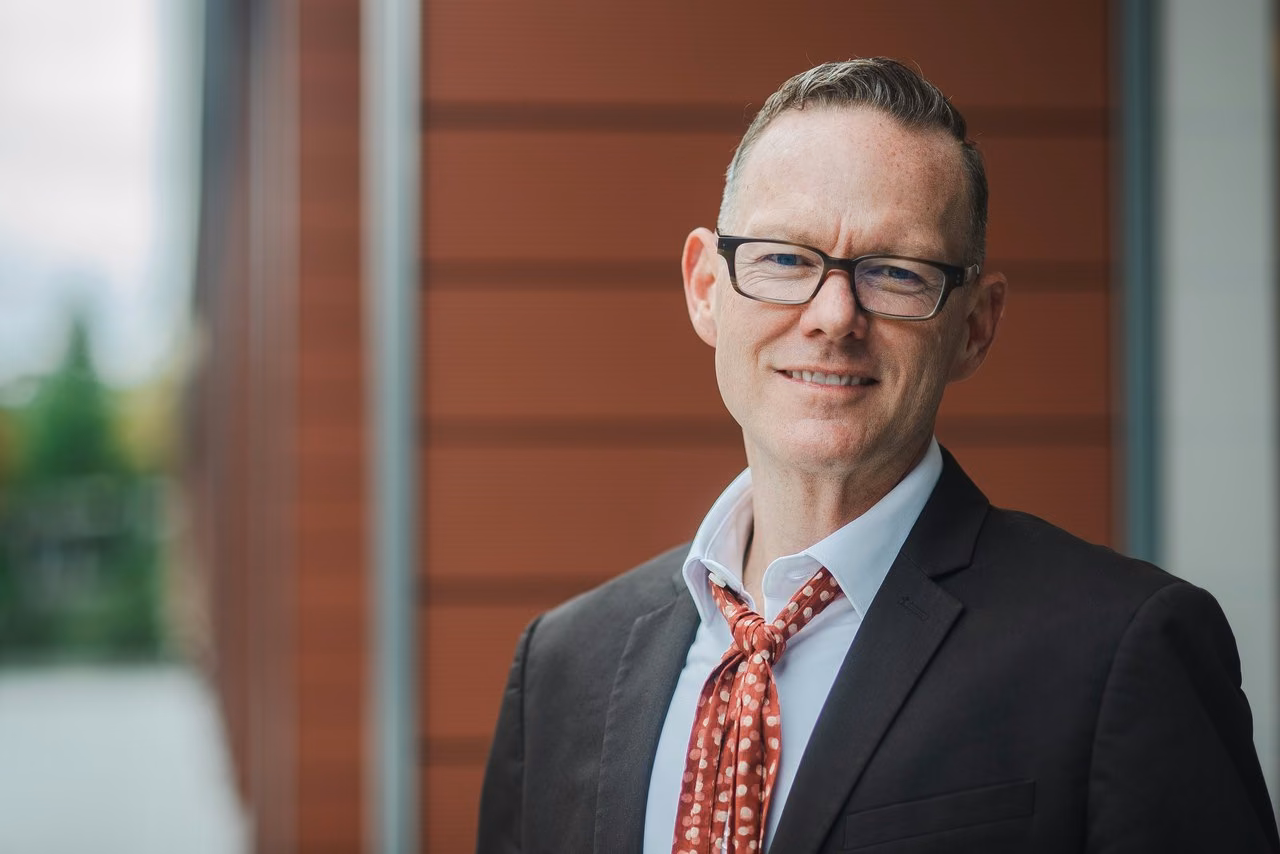 Professional team headshot of a man in a dark blazer against a neutral background