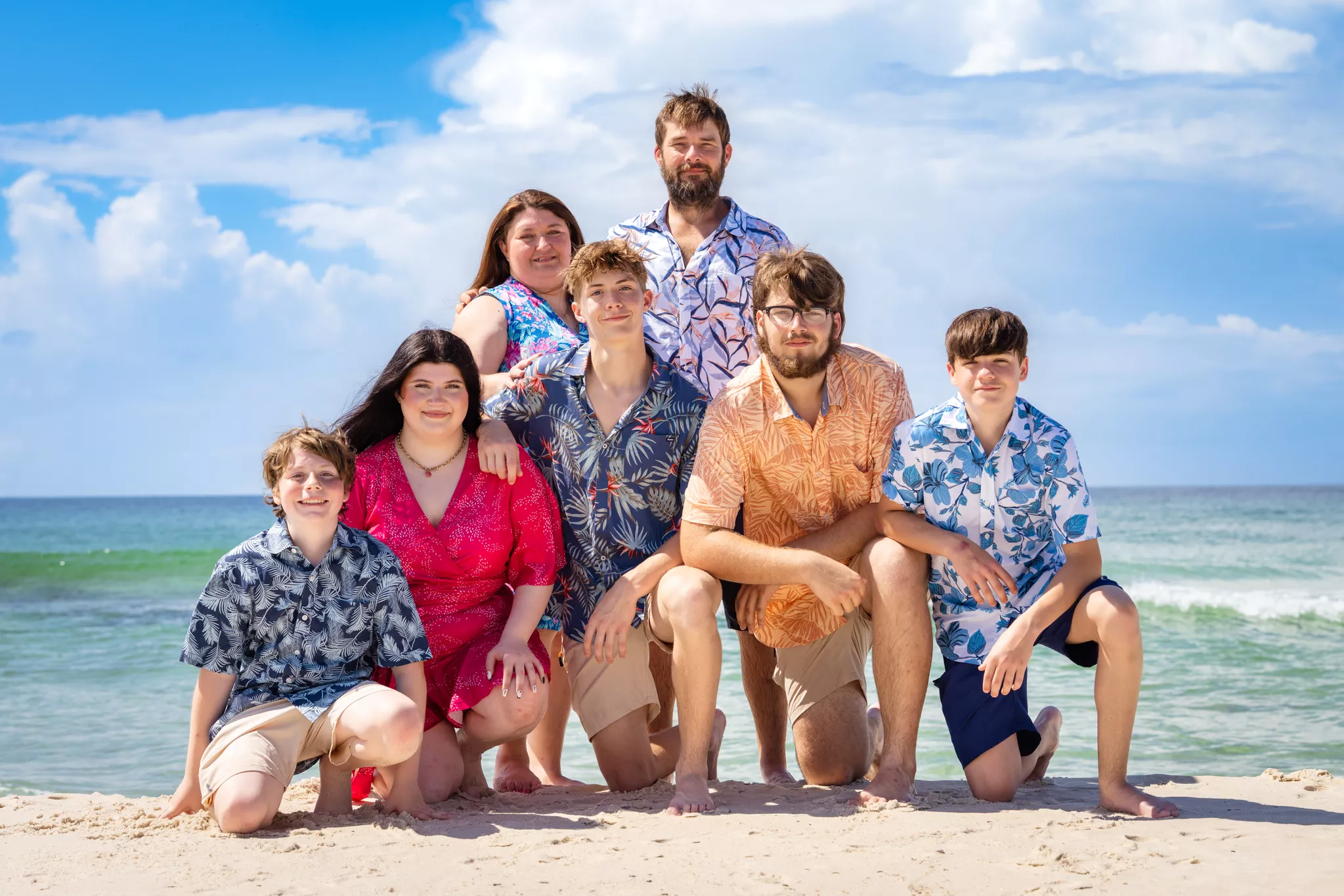 Family of seven in coordinated tropical-print photoshoot outfits on a white-sand beach