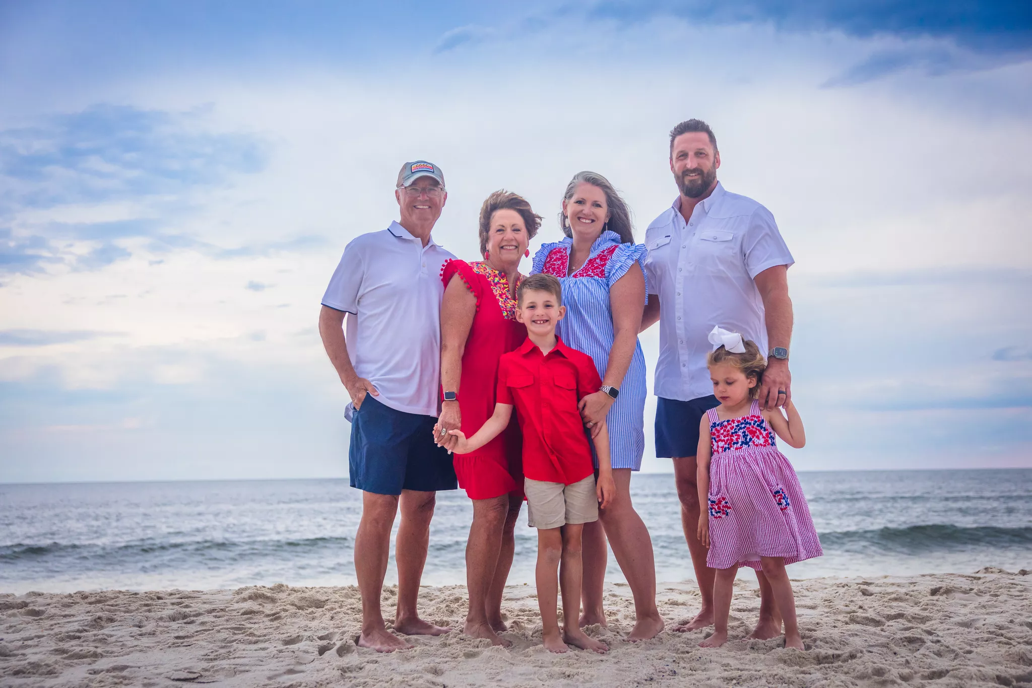 Family of six in coordinated red, white and navy photoshoot outfits on a sandy beach