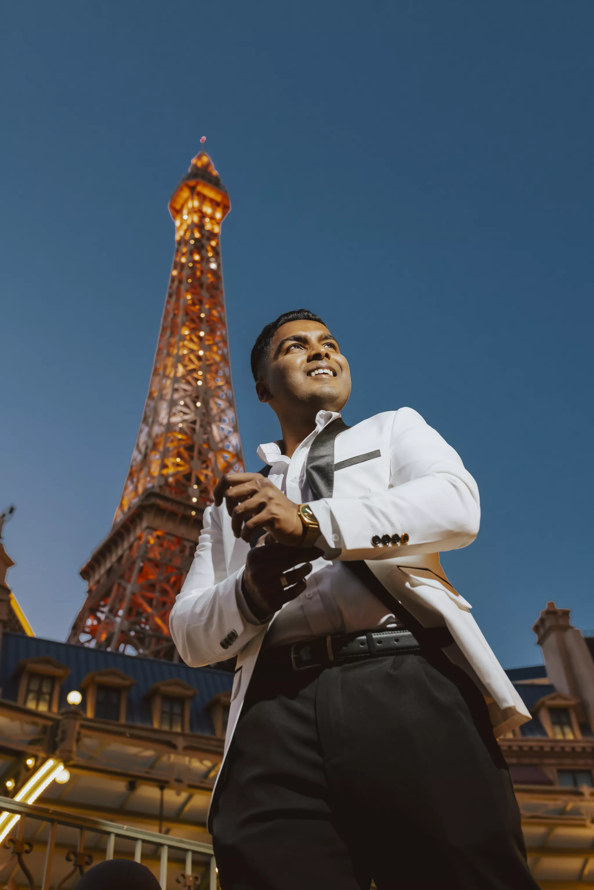 Formal photoshoot outfit of white blazer and dark tie against a lit tower at blue hour