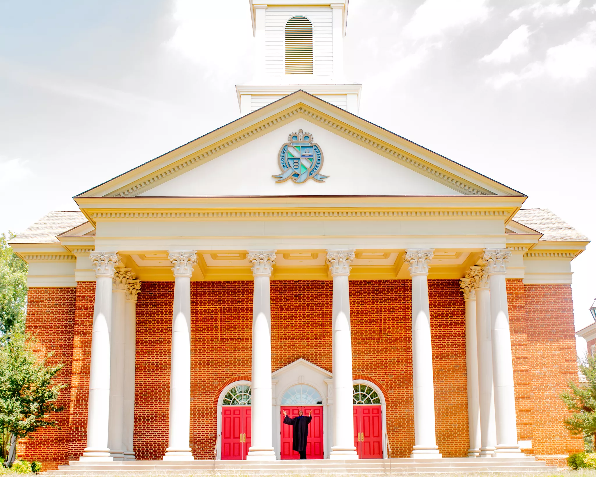 Architectural photography of a columned brick chapel, robed figure at the red doors for scale