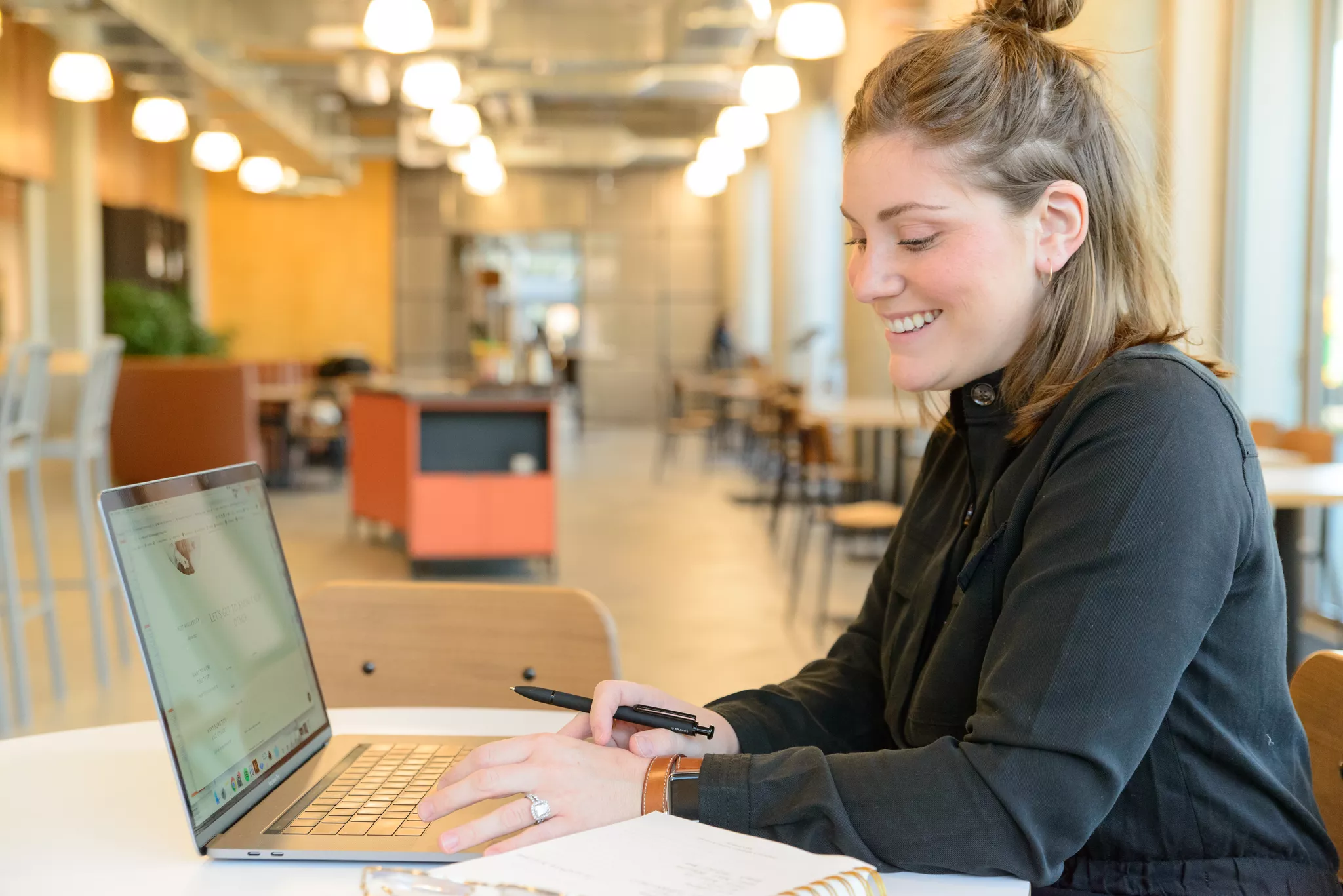 Woman smiling at a laptop in an open-plan office, a typical stock photography subject
