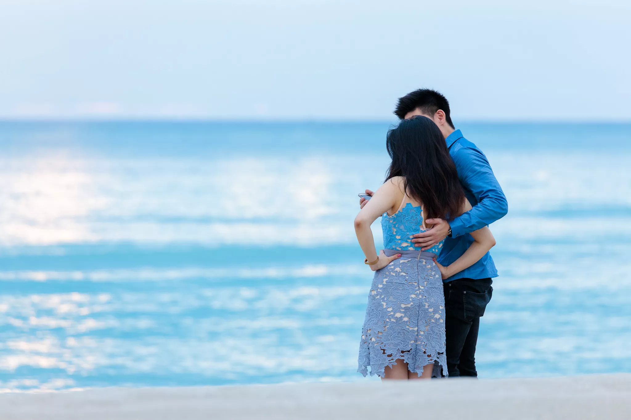 Couple embracing on a beach with their backs to camera, a generic stock photography shot