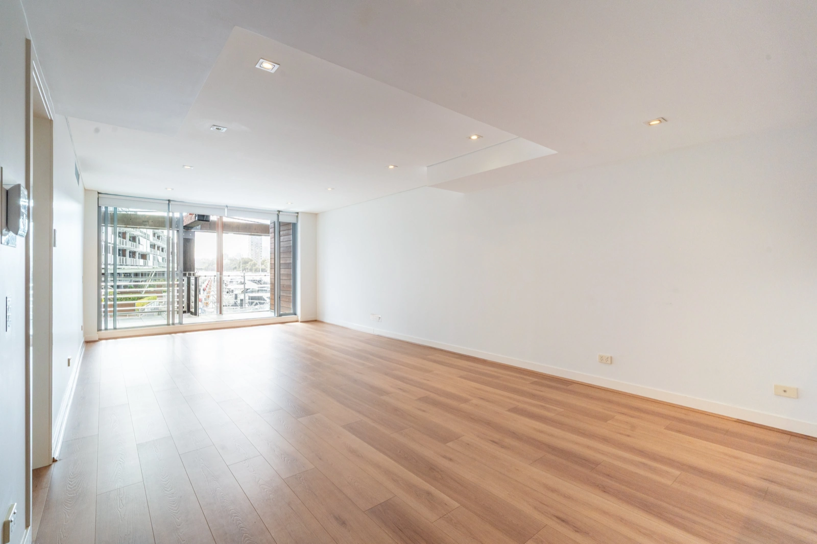 Empty apartment with bare wood floors and full-height windows, before any AI staging