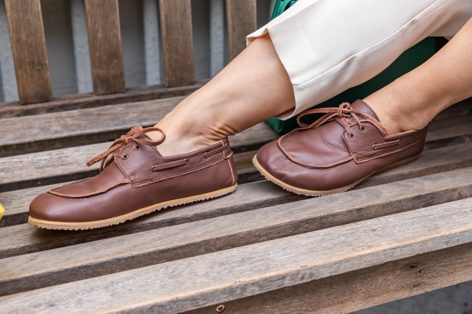 Brown leather lace-up shoes worn on a weathered wooden bench, a real product in real use
