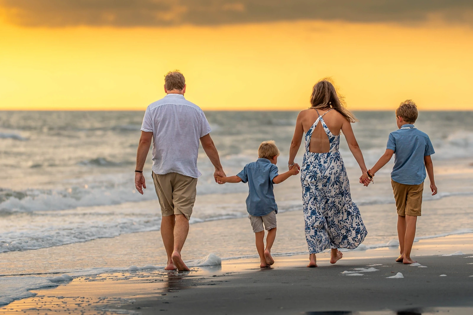 Walking family photo poses: family of four holding hands on a beach at sunset
