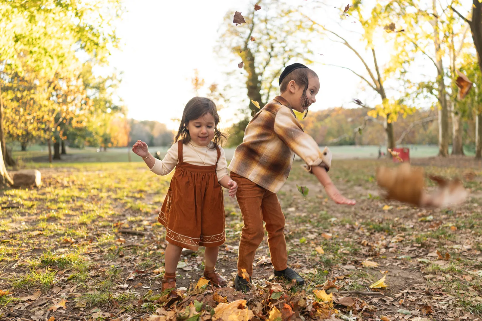 Fall family pictures idea: two kids tossing leaves in a sunlit park