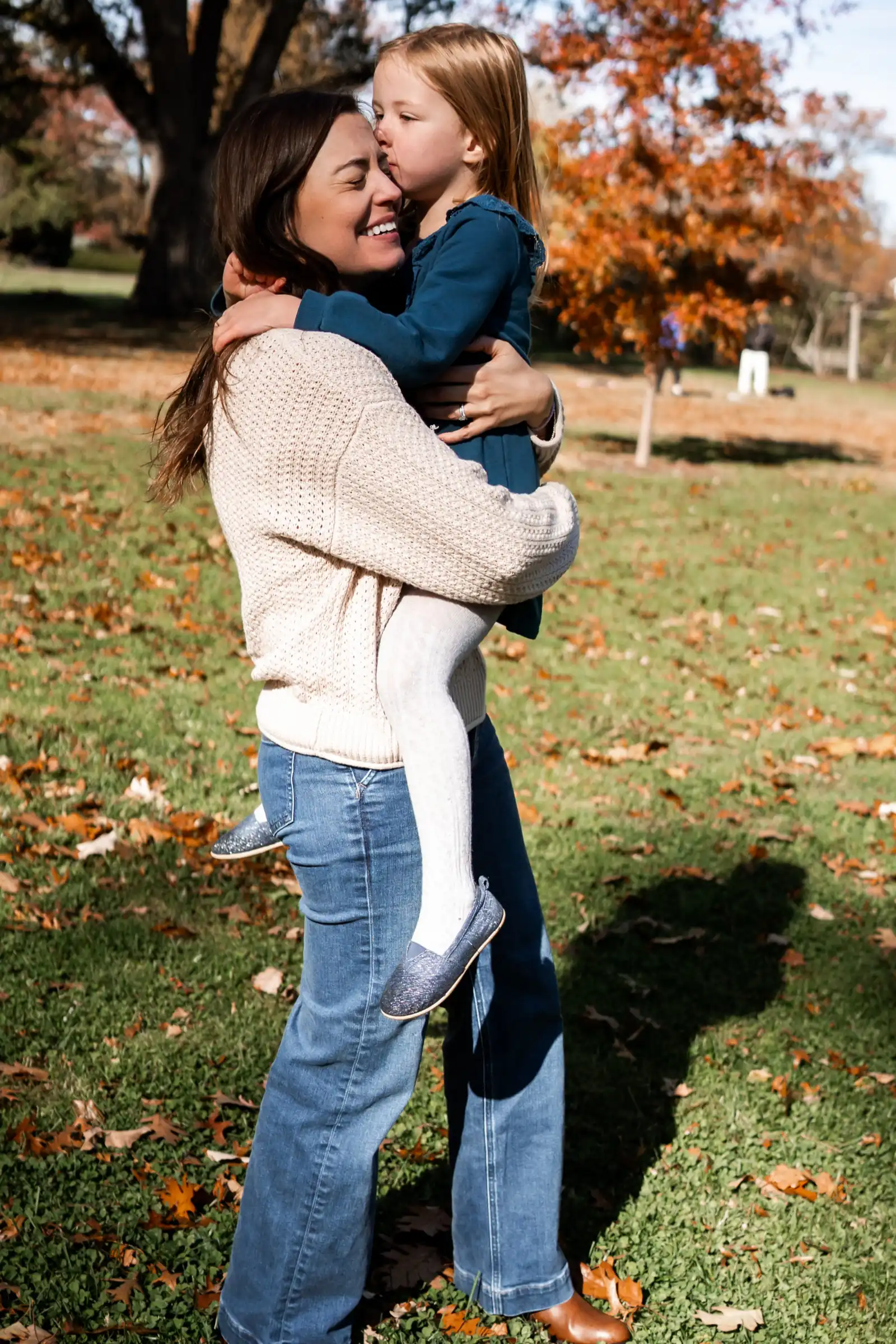 Fall family pictures in a sunny park, mom hugging daughter by orange trees