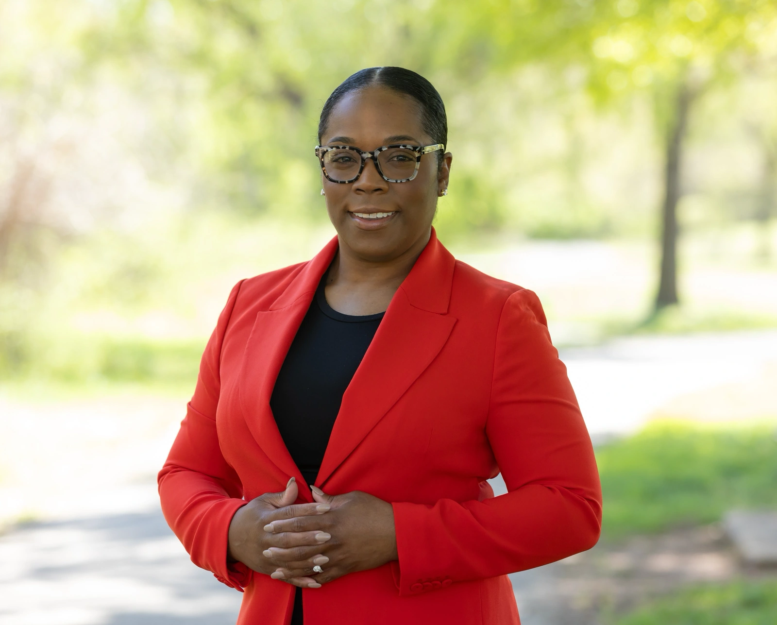 Outdoor headshot examples: woman in a red blazer on a park path with soft green blur behind.