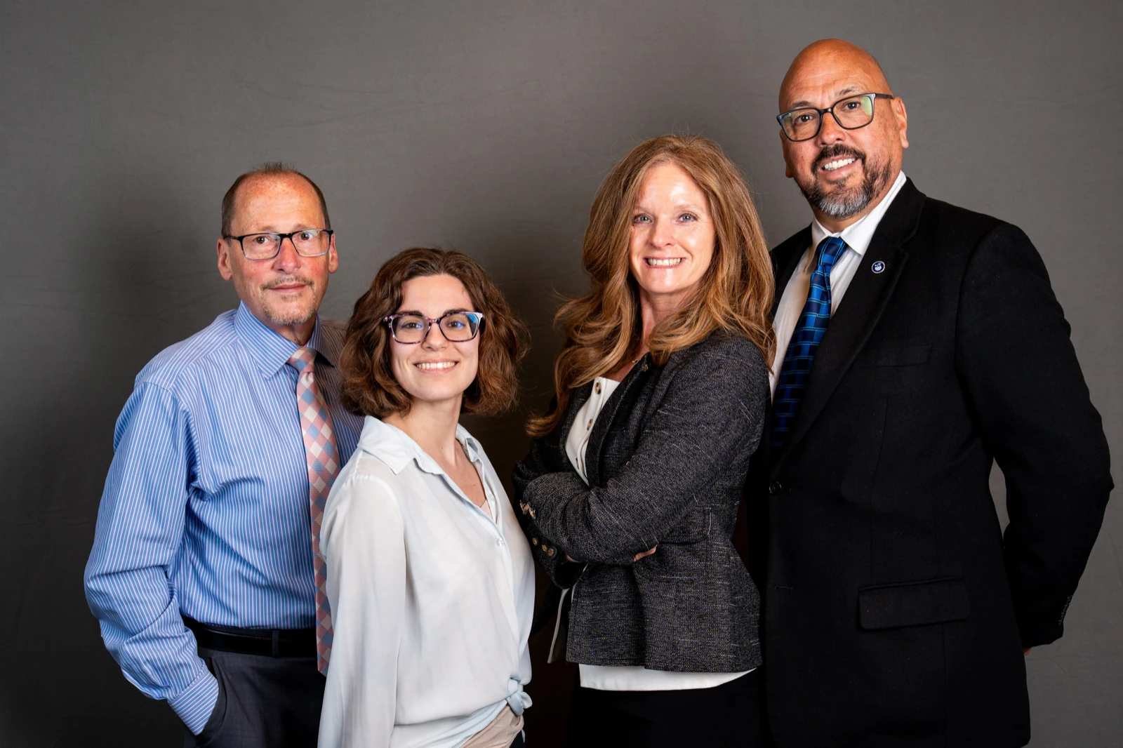 Corporate headshot examples: four colleagues on the same gray studio backdrop.