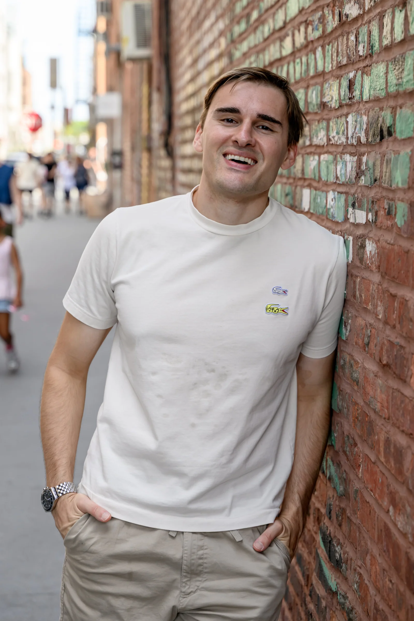 Leaning male poses: man in a white tee leaning his shoulder on a brick wall, laughing