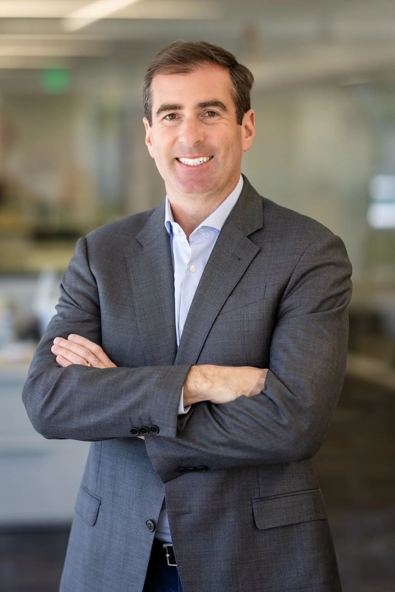 Business male poses: man in a gray suit with arms loosely crossed in an office